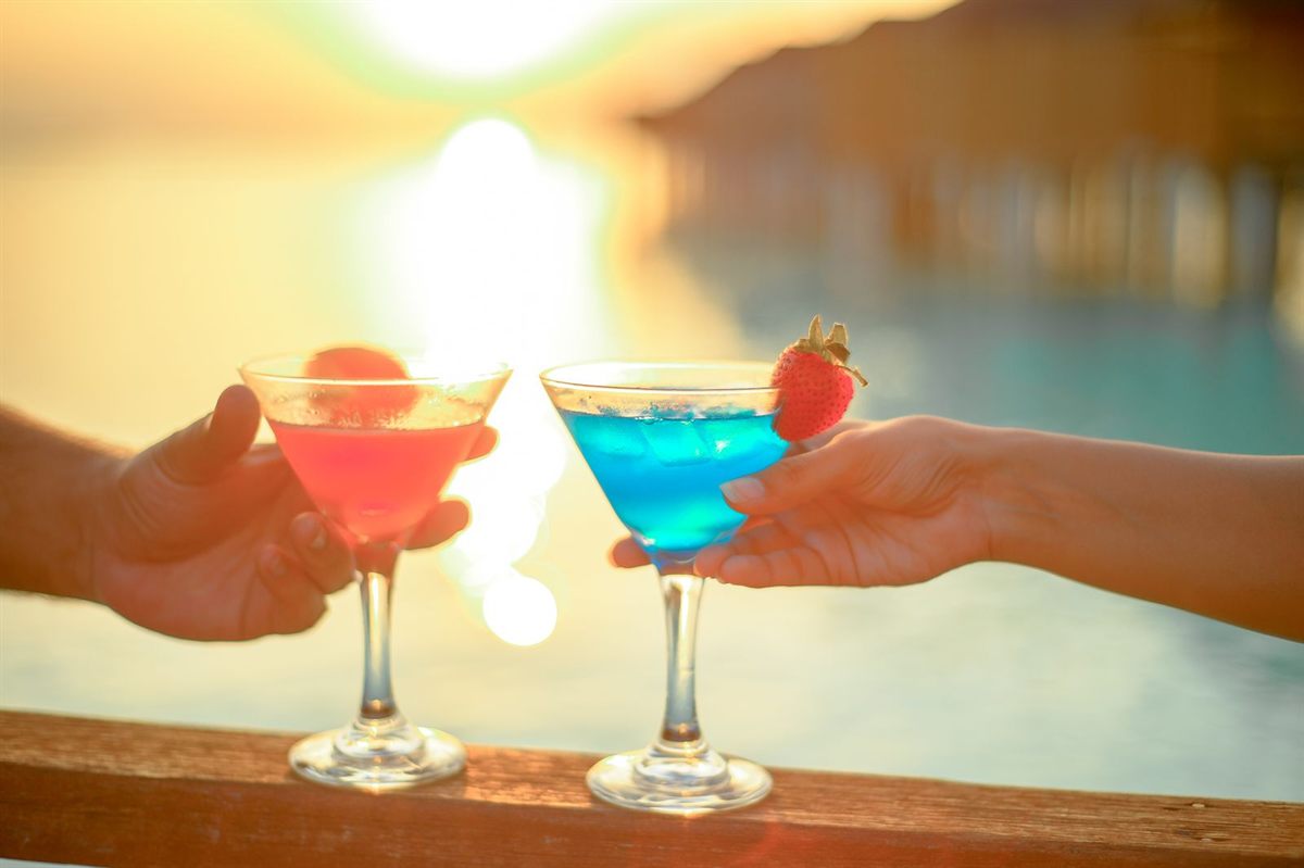 Two colourful cocktails raised against a beach sunset