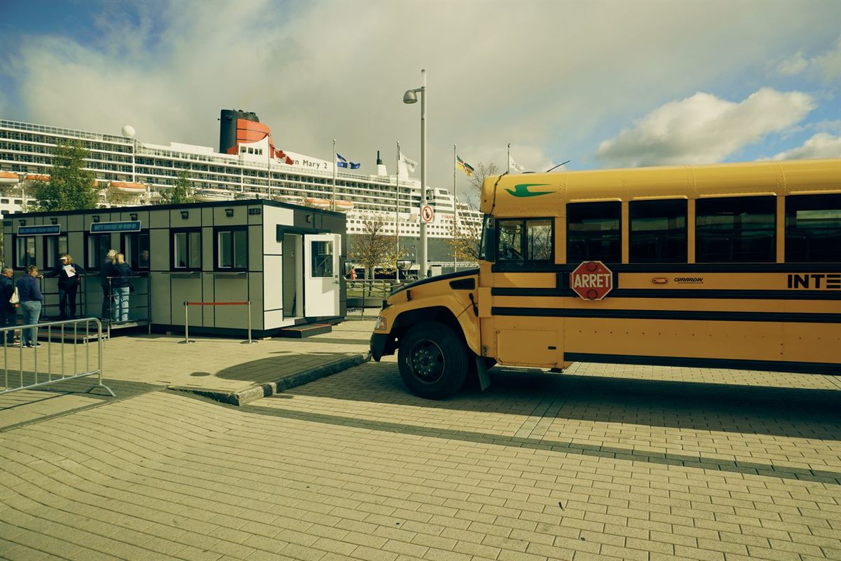 A yellow bus parked at a cruise terminal with a large ship behind it
