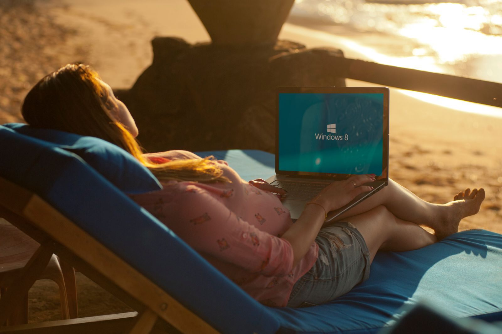 A woman on a beach lounger browsing a cruise price comparison website on her laptop